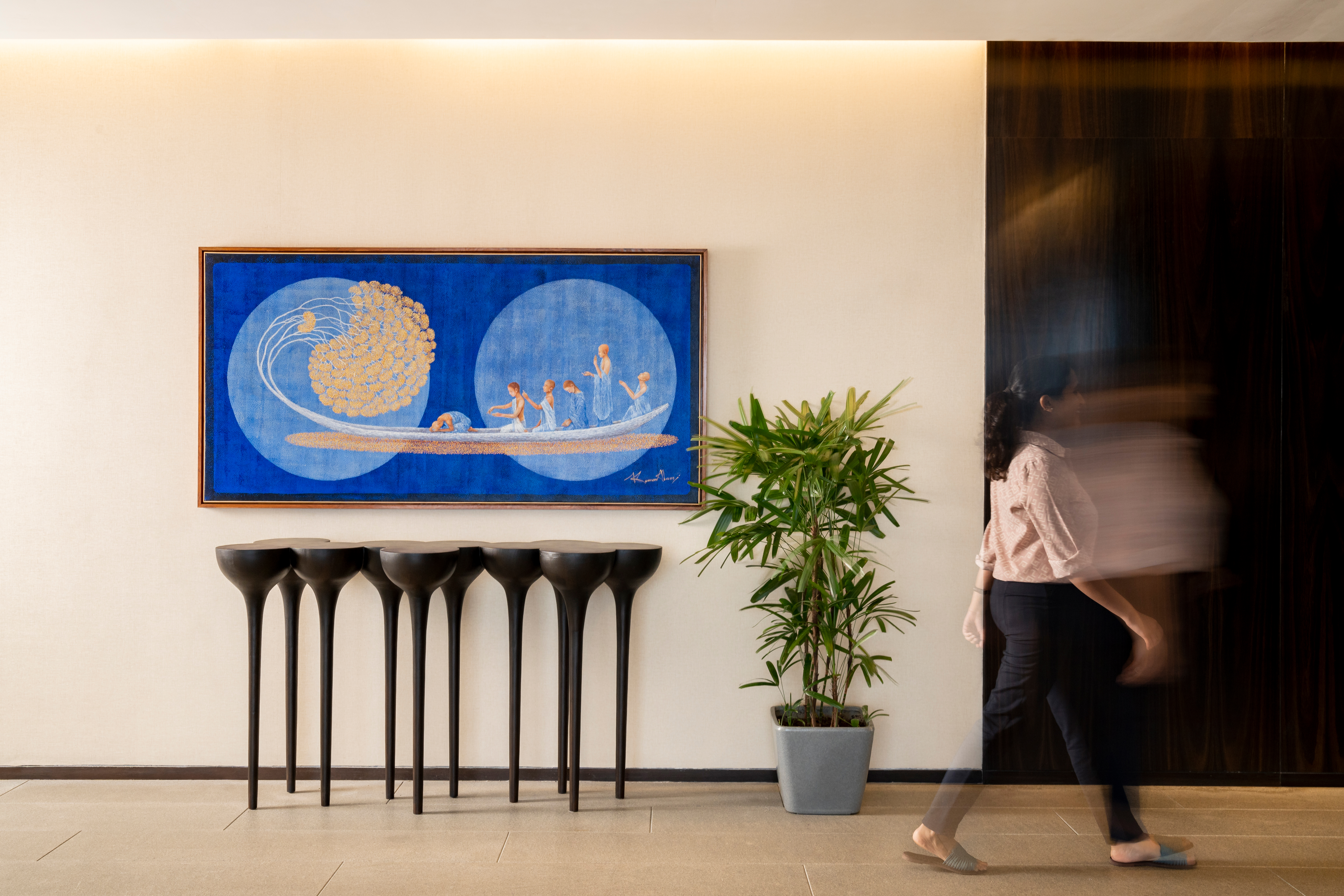 A hotel foyer with a large blue-and-gold painting, sculptural black consoles and a passing figure — Artemist Consultancy, in situ