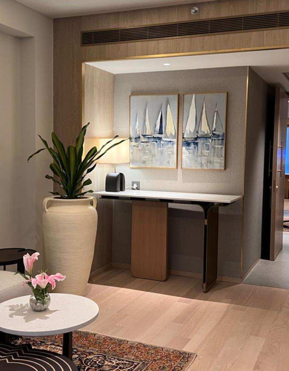 A hotel suite nook with a diptych of sailboat-and-harbour paintings above a console table — site-specific art by The Artemist, hospitality