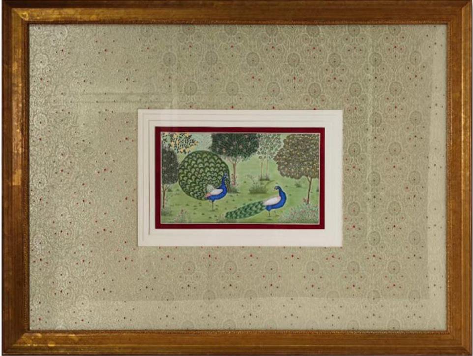 A framed Pichwai-style miniature of two peacocks in a garden, gold-mounted on a patterned wall — The Artemist, hospitality commission