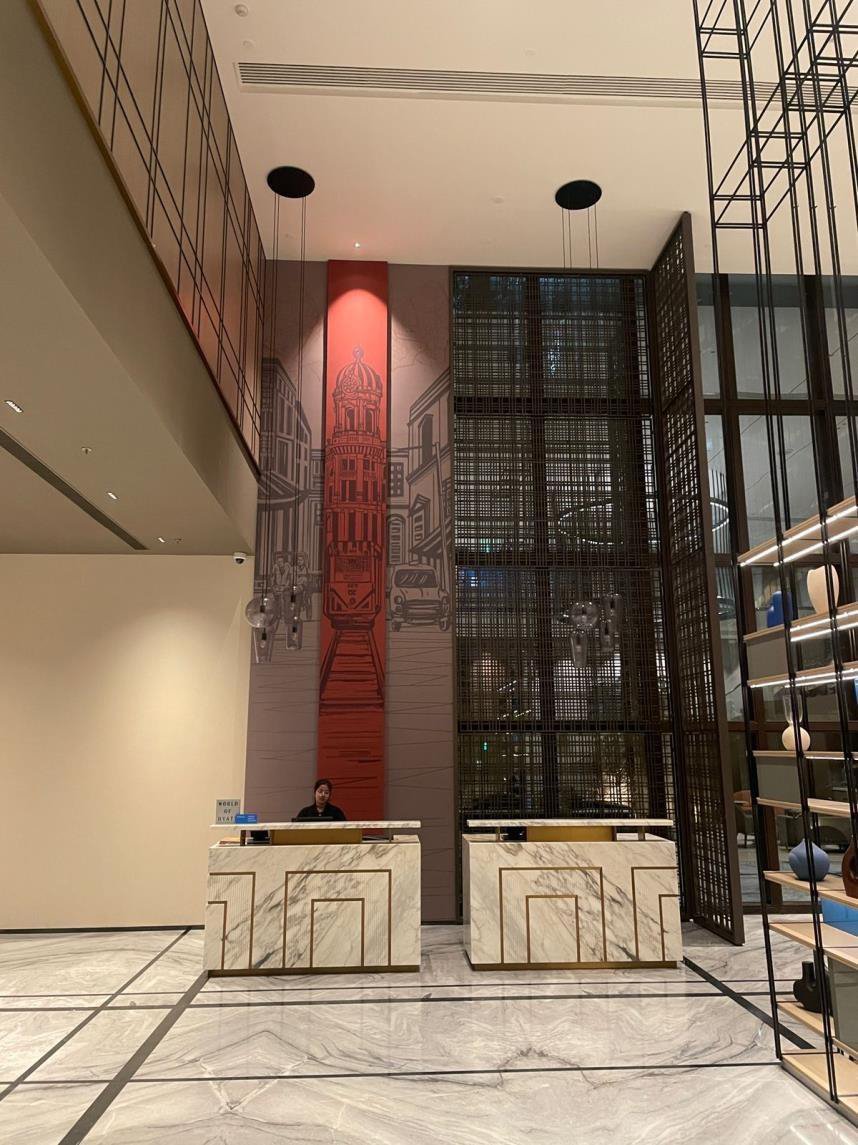 A double-height hotel lobby with a tall red-and-grey cityscape mural rising behind the reception desks — The Artemist, hospitality